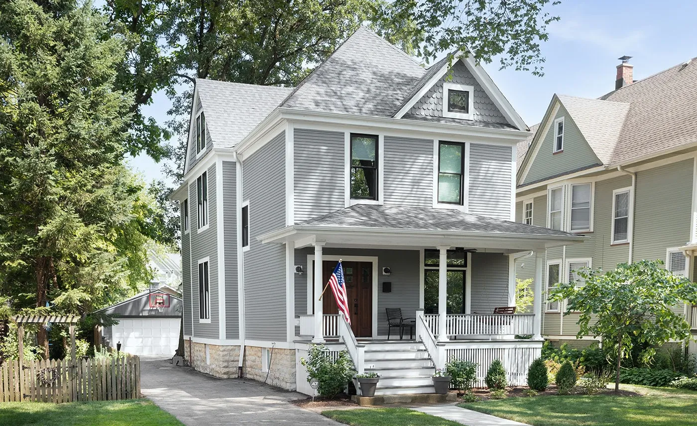 A gray two-story house with a covered front porch and an American flag