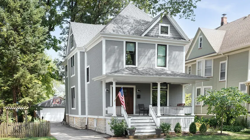 A gray two-story house with a covered front porch and an American flag